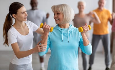 Elderly woman lifting weights with staff assistance.