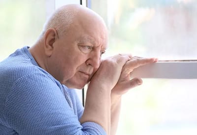 An elderly man looking contemplative by a window