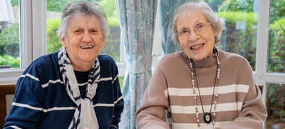 Two elderly women smiling in a bright lounge