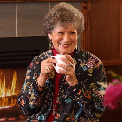 Smiling resident enjoying a warm drink by the fireplace