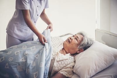 A caregiver assisting an elderly woman in bed