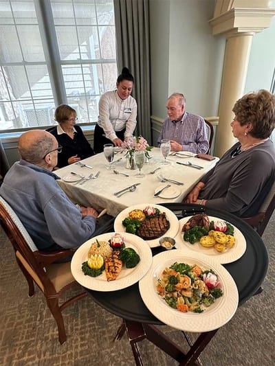 Residents enjoying a meal served by staff in the dining room