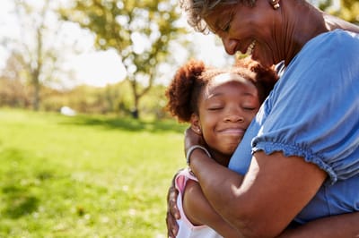 A senior woman embracing a young girl outside in a park