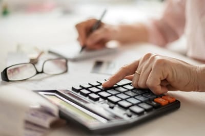 Hands using a calculator with notes and glasses in background