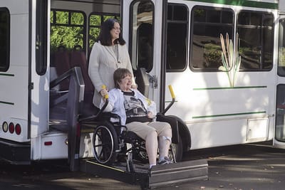 Resident in a wheelchair being assisted from a facility transport bus
