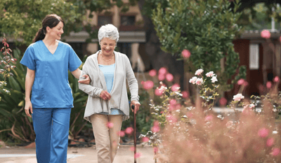 A caregiver assisting a senior woman in a garden