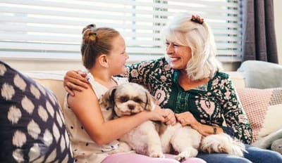 A resident and a child smiling with a dog on a couch