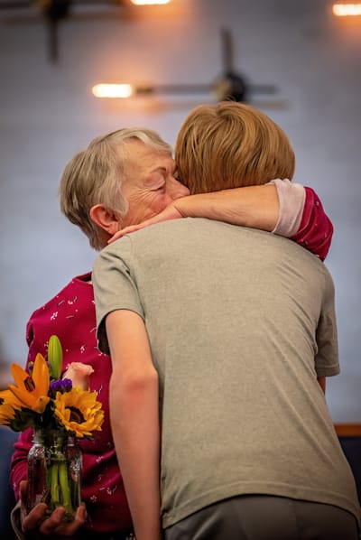 Emotional hug between a resident and a visitor with flowers