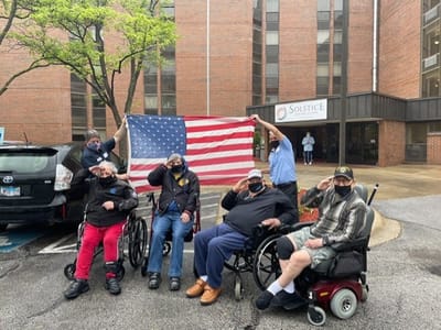 Residents saluting with an American flag in front of the facility