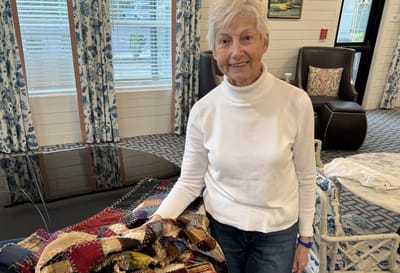 Senior resident showcasing a colorful quilt in a common area