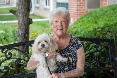 Smiling resident holding a small dog on a bench