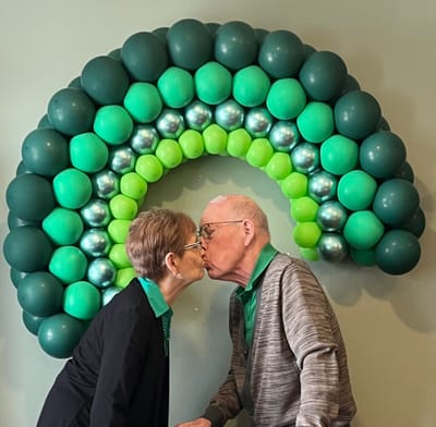 Couple sharing a kiss in front of a balloon rainbow