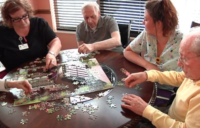 Residents and staff working on a puzzle in a common area