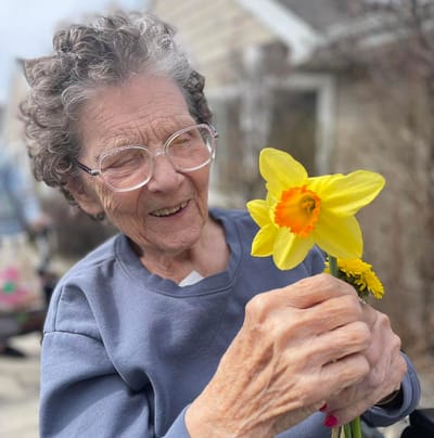 An elderly woman smiling while holding a yellow flower