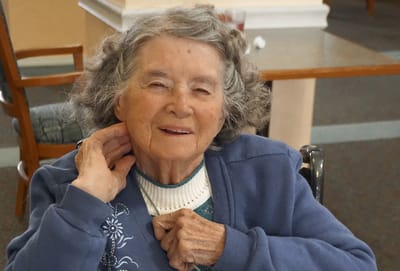 An elderly woman smiling and sitting in a common area