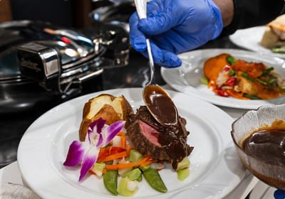 A chef plating a gourmet meal with vegetables and sauce