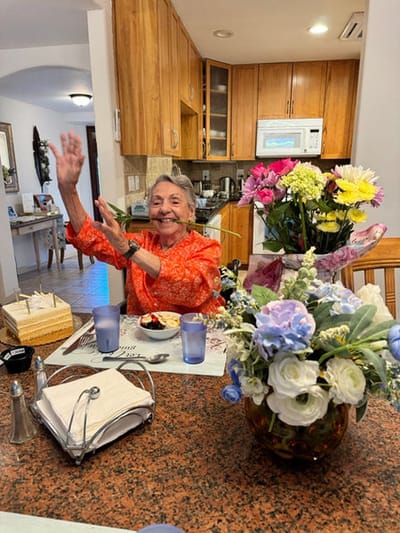 A resident smiling and waving at a dining table.