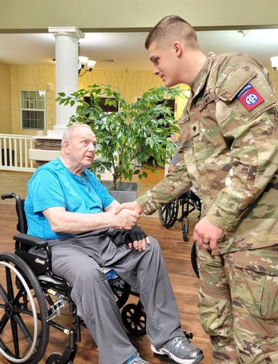 An elderly resident shakes hands with a soldier.
