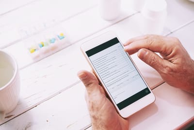 Senior using a smartphone with medication in view.