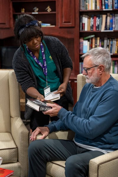Staff assisting a resident with a book in a cozy common area