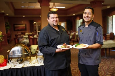 Two chefs presenting plates of food in the dining area