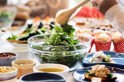 A hand preparing a salad at a dining table
