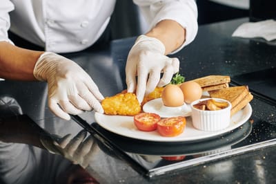 A chef plating a breakfast meal with eggs and vegetables