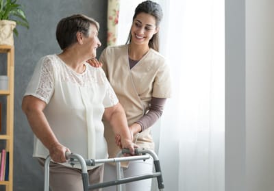 Caregiver assisting a resident with a walker indoors.