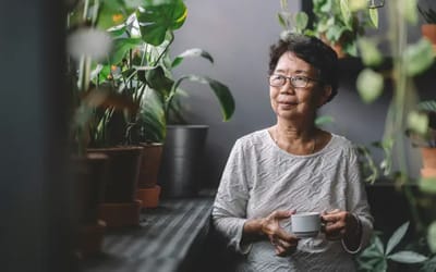 Senior woman enjoying a cup in a plant-filled interior.