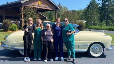 Staff and resident posing outside the facility with a vintage car