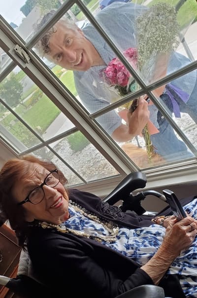Resident smiling with a visitor holding flowers