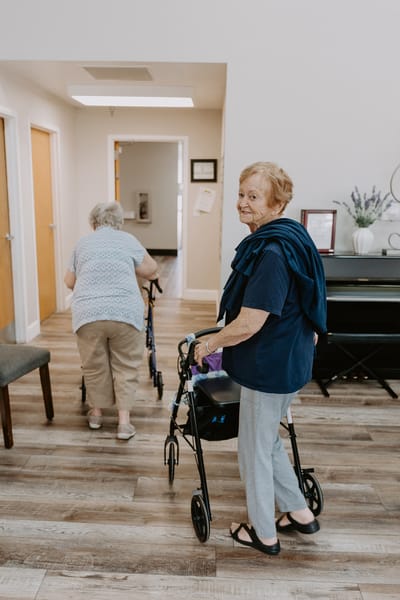 Two elderly residents using walkers in a hallway