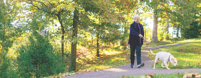 Senior woman walking her dog on a path in a garden