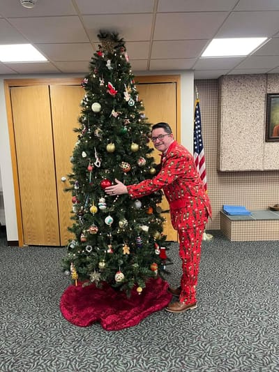 Staff member in festive attire by a Christmas tree