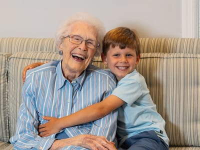 An elderly woman and a young boy smiling together on a couch