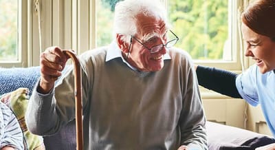Staff member assisting a smiling resident indoors
