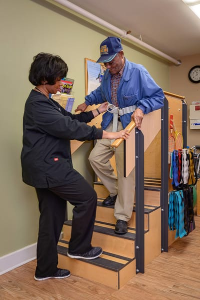 Staff assisting a resident on stairs in an interior space