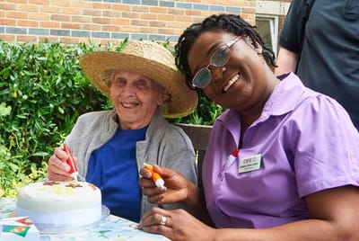 Staff and resident celebrating with a cake outdoors