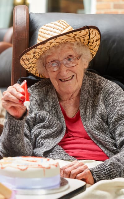 A smiling elderly woman with a cake celebrating her birthday