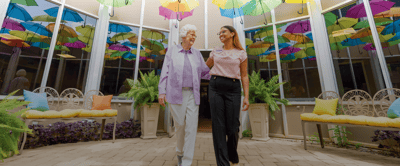 Staff walking with a resident in a colorful atrium