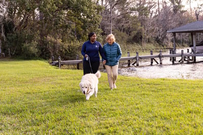 Staff member and resident walking a dog by the water