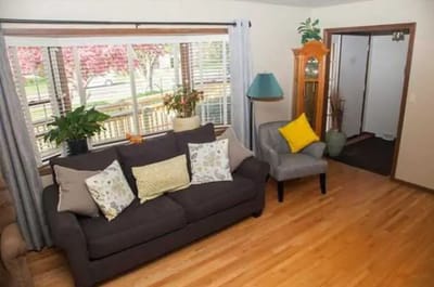 Living room with a sofa, armchair, and large windows letting in natural light.