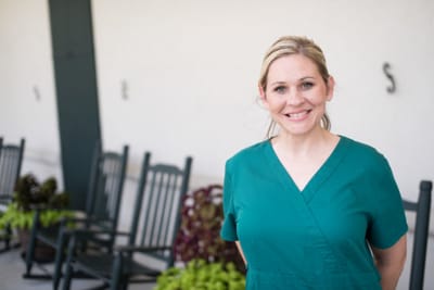 Nurse smiling in front of rocking chairs outdoors.