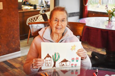 Resident holding a colorful drawing in a bright room