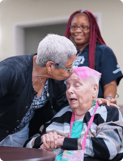 A caregiver kissing a resident with colorful hair
