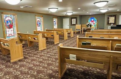 Interior view of a chapel with wooden pews and stained glass windows