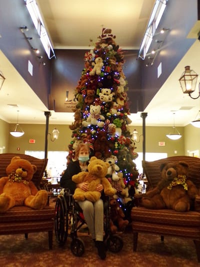 Resident with teddy bears by a decorated Christmas tree