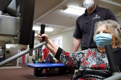 A resident exercising in a common area with staff assistance