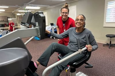 Resident exercising with staff assistance in a gym area