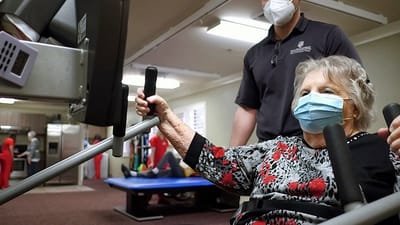 Senior resident using exercise equipment with staff assistance